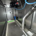 Válvula actuada instalada en una línea de acero inoxidable dentro de una cabina industrial, con conexiones neumáticas y tubería soldada por Soldaduras Dad