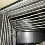 Conjunto de tuberías industriales de acero conectadas a un depósito, con trazado paralelo y uniones soldadas para proceso industrial preparado por Soldaduras Dad, expertos en soldadura y sistemas de fluidos en Zaragoza